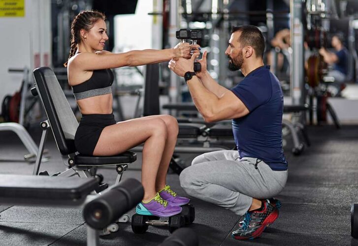 Personal trainer assisting young woman in the gym