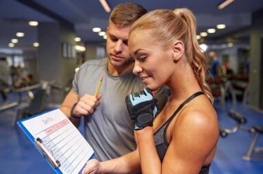 Smiling woman with trainer and clipboard in gym