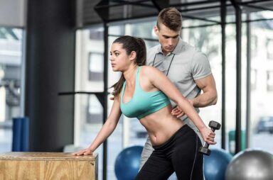 Male trainer assisting woman lifting dumbbells