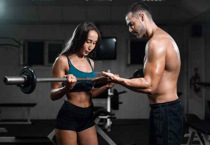 Man instructor and woman train in the gym, lifting dumbbells