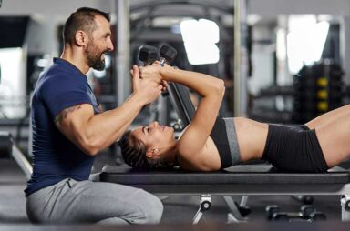 Personal trainer helping woman with triceps workout in the gym