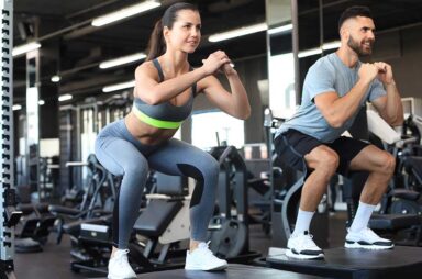 Fit couple doing jumping squats in crossfit gym