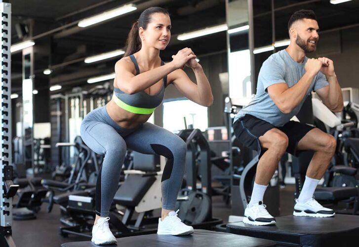 Fit couple doing jumping squats in crossfit gym