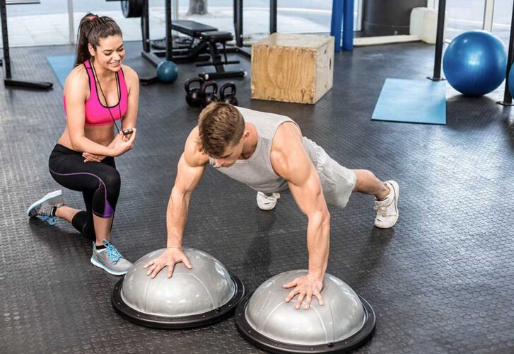 Man working out helped by trainer woman