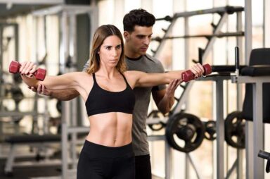 Personal trainer helping a young woman lift weights