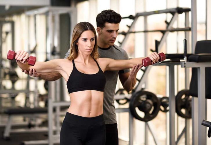 Personal trainer helping a young woman lift weights