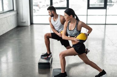 Side view of sportive young couple holding medicine balls and exercising on step platforms in gym