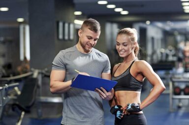 Smiling young woman with personal trainer in gym