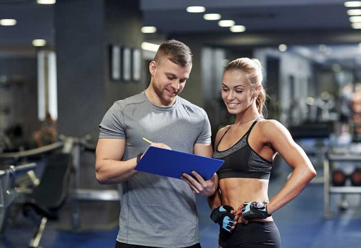 Smiling young woman with personal trainer in gym