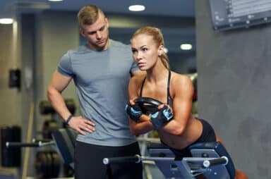 Woman with personal trainer flexing muscles in gym