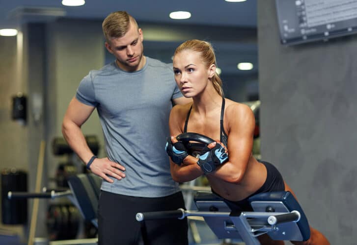 Woman with personal trainer flexing muscles in gym