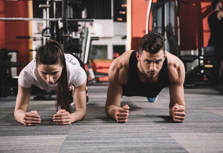 Attractive trainer doing plank exercise together