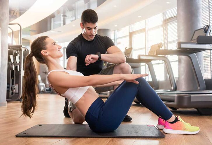 Personal trainer timing young fit woman during isometric exercis