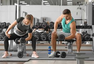 Sporty young couple training with dumbbells in gym
